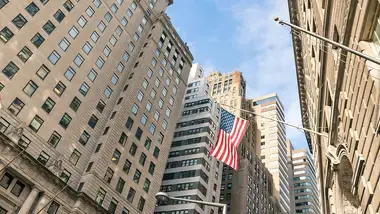 Looking up from the street at skyscrapers with an American flag displayed on one.